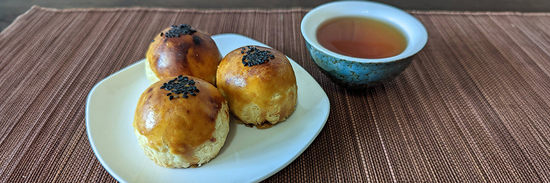 Three mooncakes on a plate next to a cup of oolong tea