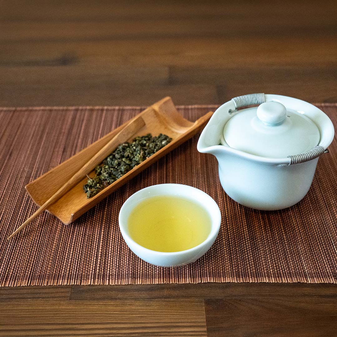 Gaiwan Pitcher with Handles with tea leaves and tea cup sitting on a wooden table