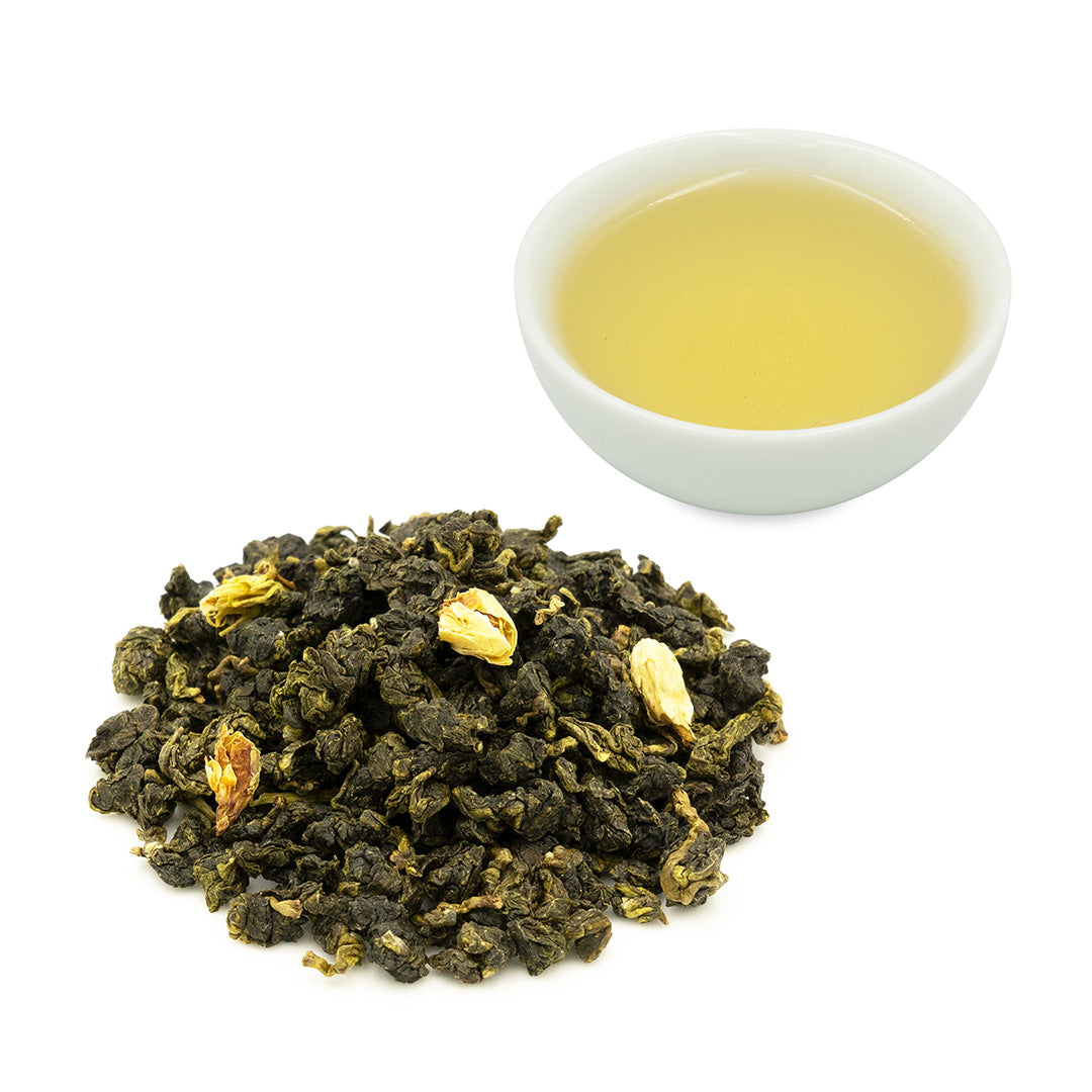 Jasmine Flower Green Tea dry leaves in a pile next to a cup of brewed tea in a white tea cup.