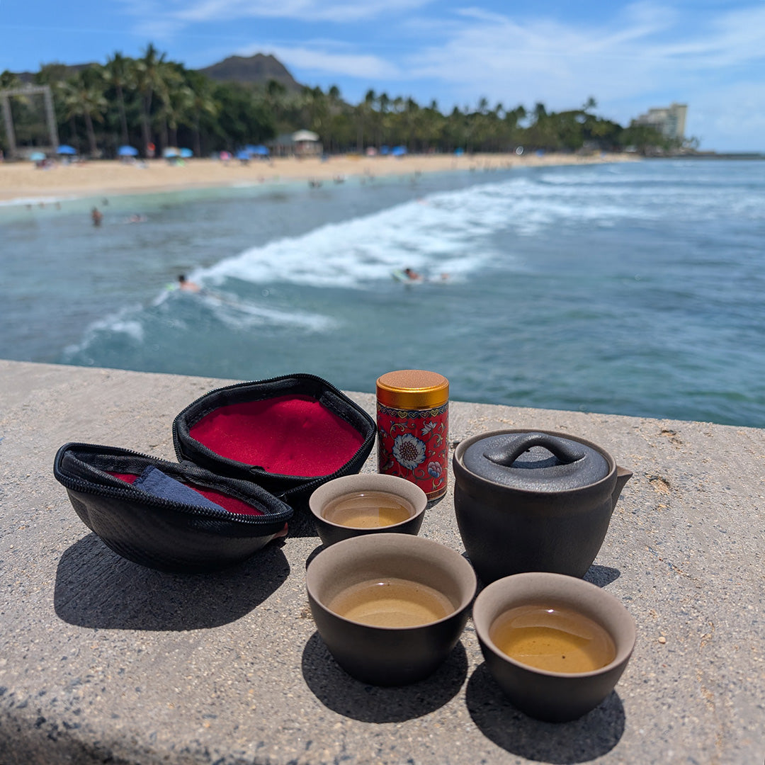 Eco-Cha Travel Tea Set on a concrete ledge overlooking the surf with surfers and Diamond Head in the background.