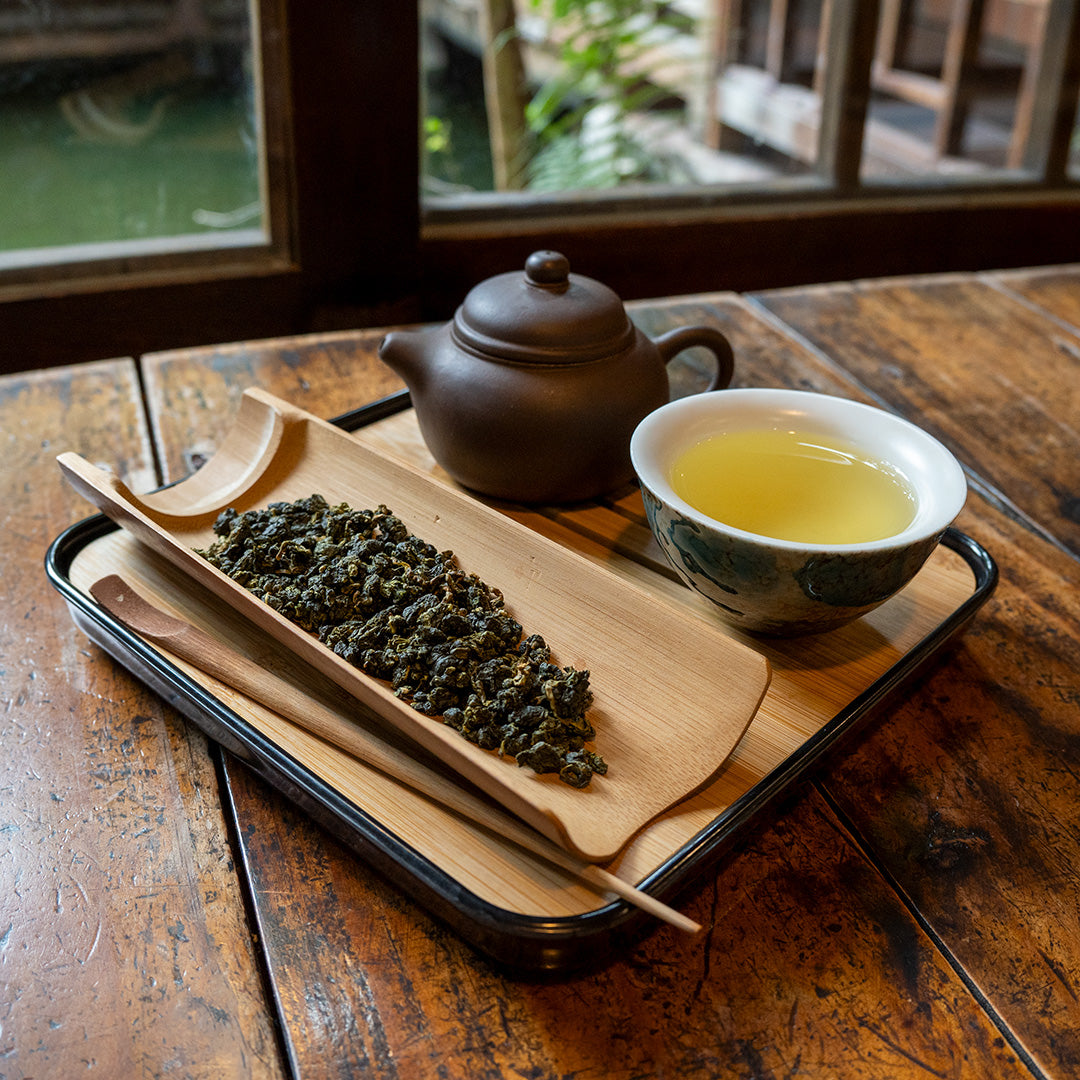 Bamboo Tea Scoop and Tea Pick on a tea tray with a tea pot and a cup of tea on a wooden table