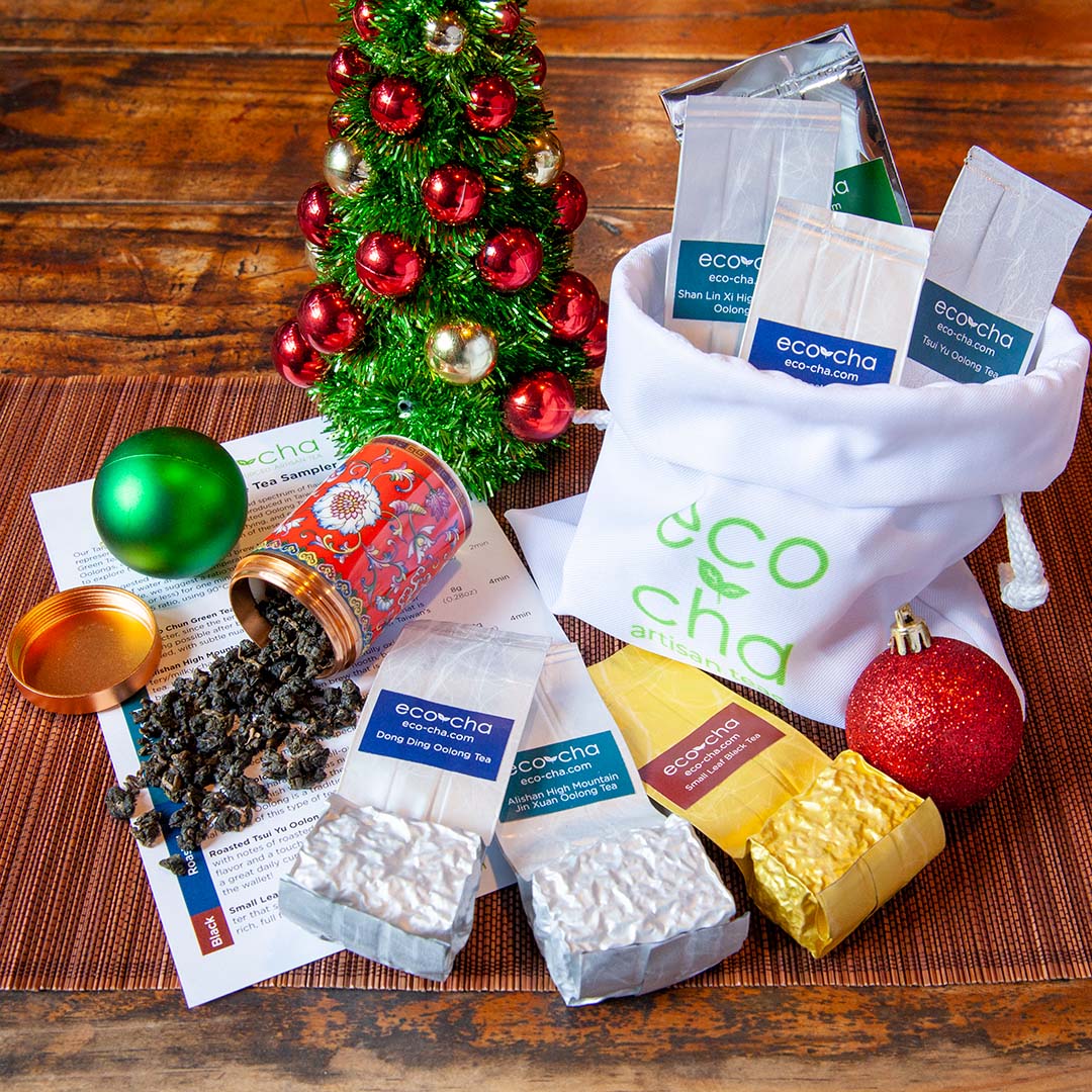 Taiwanese Tea Sampler on a wooden table with small decorated Christmas tree by the side.  Seven packets of tea samples are neatly arranged next to some dried tea leaves spilling out from a red tea caddy.