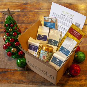 Box of Eco-Cha Holiday Sampler with a small Christmas tree and ornaments on a wooden table.