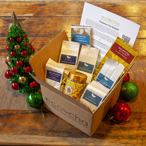 Eco-cha Tea Sampler box with tea bags, a yellow ceramic tea caddy, and decorative items on a wooden surface.
