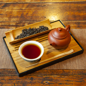 Bamboo tea tray with dry tea leaves and tea in cup with red tea pot on an old wooden table