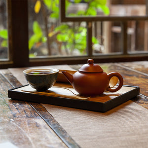 Bamboo tea tray on old wooden table with tea pot and tea cup next to a window overlooking a garden