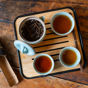 Portable Bamboo Tea Tray with three cups of tea and a tea pot all sitting on a wooden table as seen from directly above looking down.