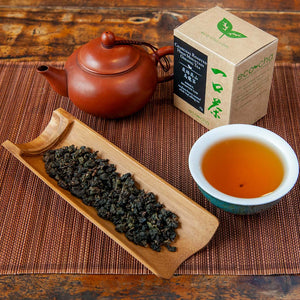 Charcoal Roasted High Mountain Oolong Tea brewed with dry leaves on a table next to a brown teapot and packaging box