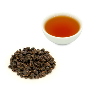 Charcoal Roasted High Mountain Oolong Tea, brewed in a teacup behind some dry tea leaves