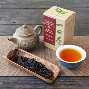 Eco-Farmed Four Seasons Spring Black Tea brewed in a cup and with dry leaves and packaging on a wooden table.