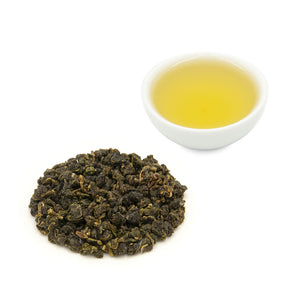 Eco-Farmed Four Seasons Spring Oolong Tea by Eco-Cha Teas brewed in a cup alongside a pile of dry, rolled, tea leaves.