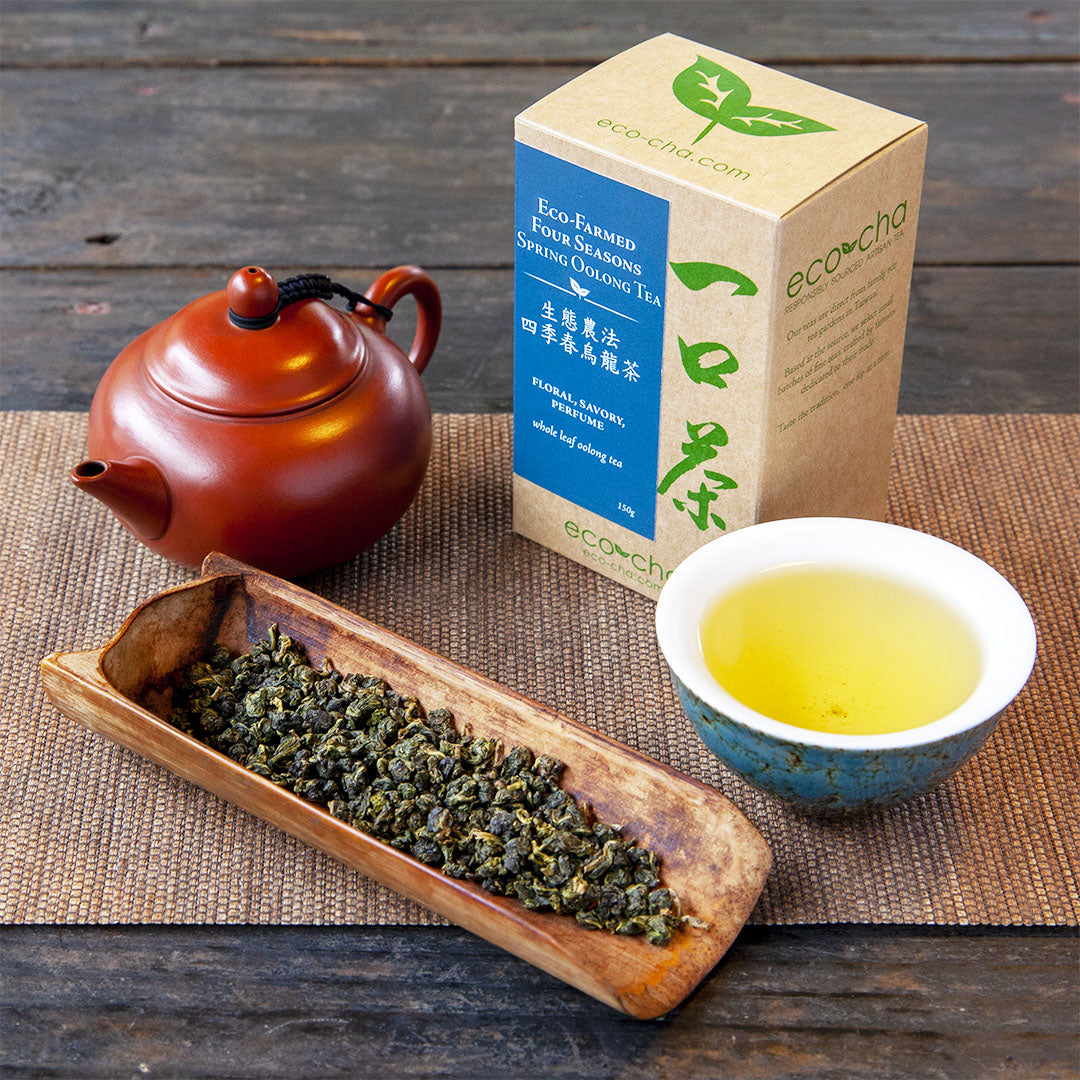 Eco-Farmed Four Seasons Spring Oolong Tea, brewed tea in cup alongside dry leaves, packaging and a red teapot.