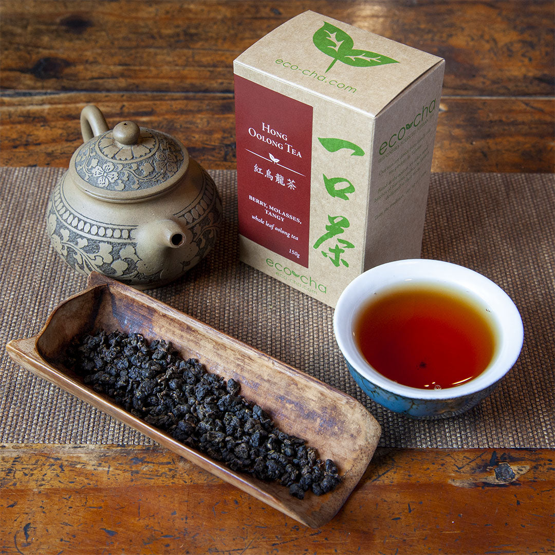 Hong Oolong Tea, dry leaves in a scoop next to brewed tea in a cup alongside package box and teapot