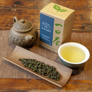 Jin Xuan Oolong Tea in teacup on wooden table next to dry tea leaves and old teapot and box