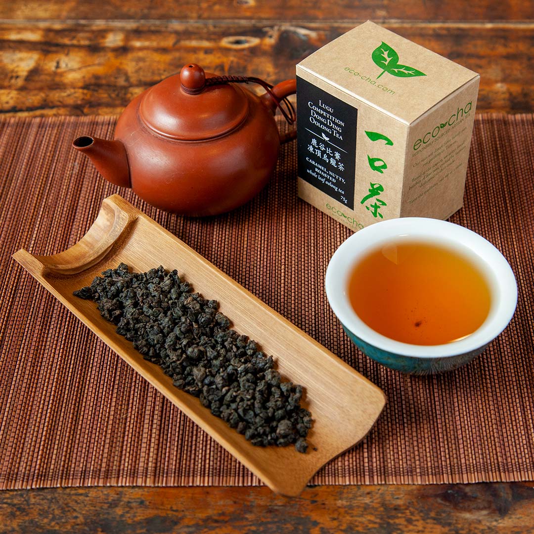 Taiwan Lugu Limited Edition Dong Ding Oolong Tea on a tea scoop alongside brewed tea and packaging and tea pot