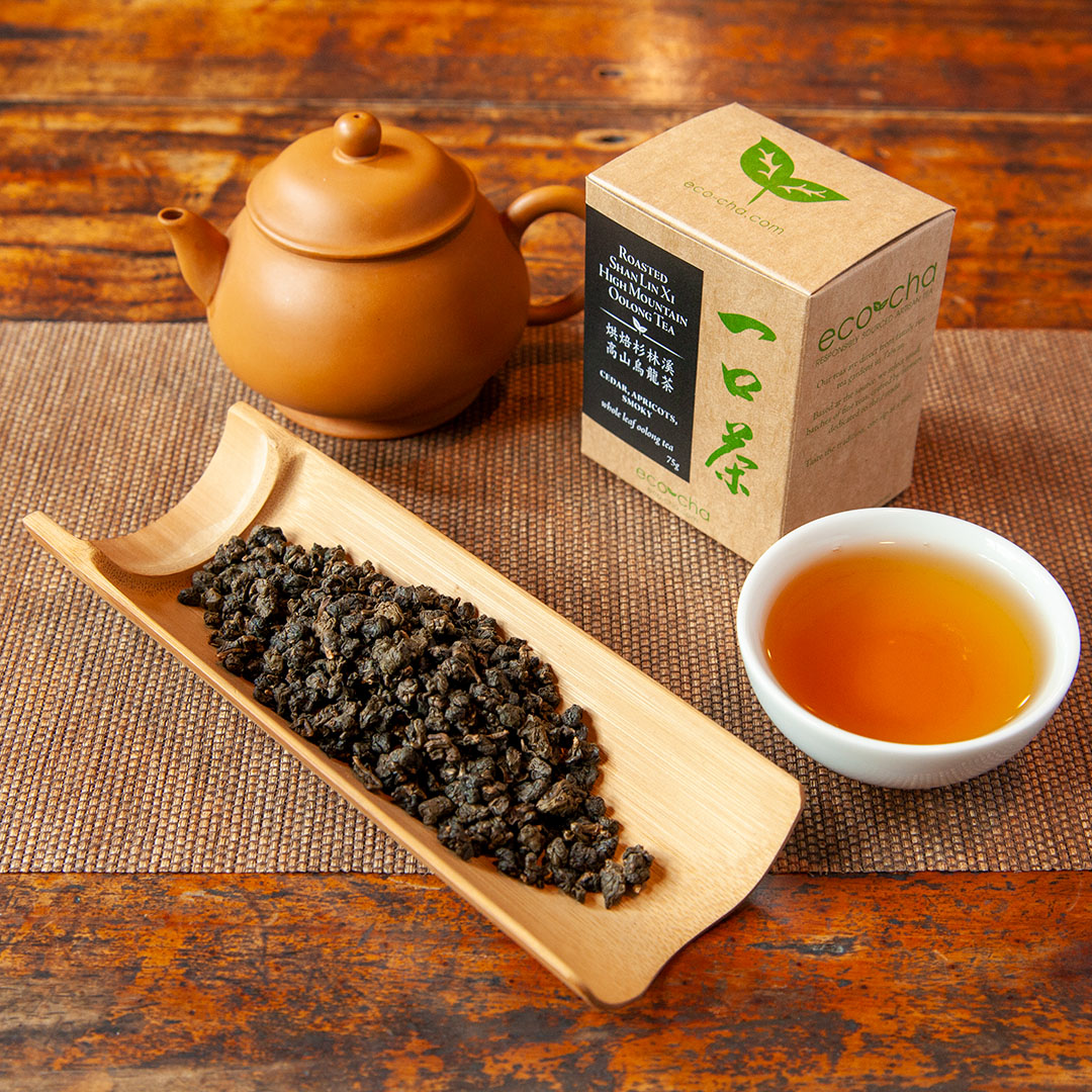 Eco-Cha Teas Roasted Shan Lin Xi  High Mountain Oolong Tea on a wooden table next to a cup of brewed tea, package box and a tea pot.