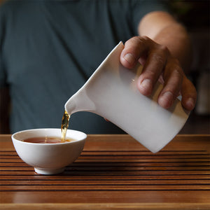 White porcelain tea pitcher pouring tea into white cup