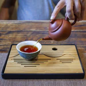 Portable bamboo tea tray with tea cup and teapot pouring tea
