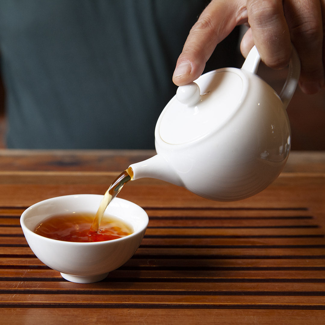 Pouring tea with white porcelain gong-fu teapot into white cup